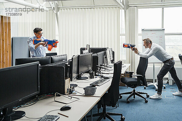 Männliche Kollegen spielen mit einer Spielzeugpistole  während sie am Schreibtisch stehen