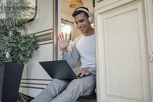 Lächelnder männlicher Freiberufler  der während eines Videoanrufs über einen Laptop mit der Hand winkt
