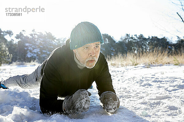 Aktiver Mann mit Strickmütze bei einer Plank-Übung auf Schnee im Winter