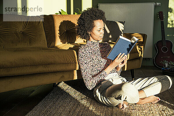 Frau  die im Schneidersitz zu Hause ein Buch liest