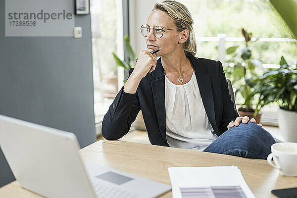 Weibliche Fachkraft mit Hand am Kinn  die im Büro sitzt und nachdenkt