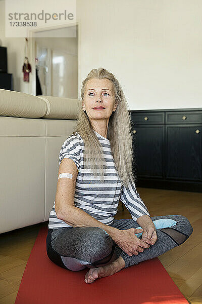Österreich  Wien  Ältere Frau mit Pflasterverband am Arm auf Yogamatte sitzend