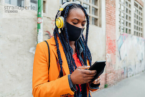 Italien  Mailand  Frau mit Kopfhörern und Gesichtsmaske hält Smartphone