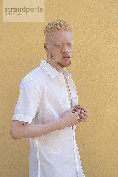 Deutschland  Köln  Albino-Mann im weißen Hemd vor gelber Wand