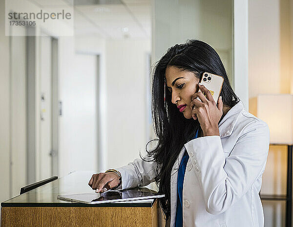 Arzt telefoniert an der Rezeption mit dem Mobiltelefon