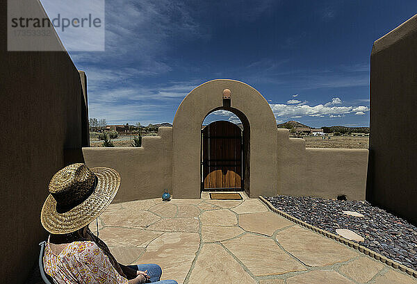 USA  New Mexico  Santa Fe  Seniorin mit Strohhut sitzt auf der Terrasse neben dem Haus