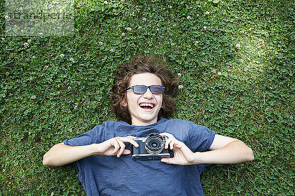 Junge liegt mit Kamera im Gras