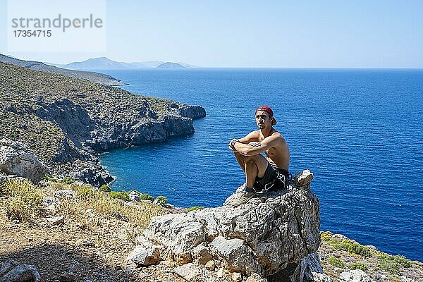 Junger Mann sitzt auf einem Felsen an der Küste  Kalymnos  Dodekanes  Griechenland  Europa