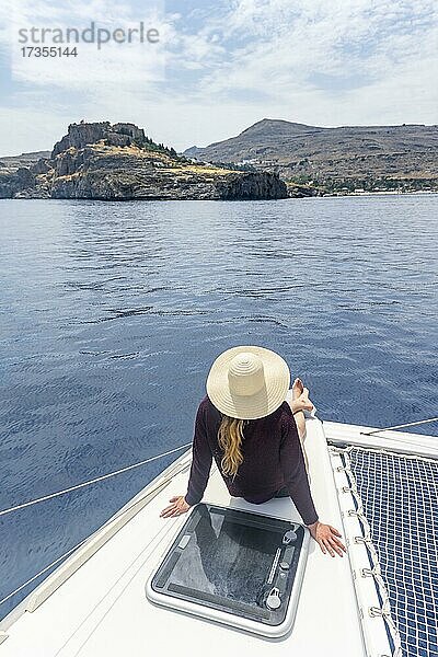 Junge Frau mit Sonnenhut sitzt auf einem Boot  Lindos  Rhodos  Dodekanes  Griechenland  Europa