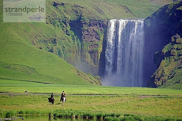 Reiterinnen vor Wasserfall  grüne Landschaft und Berge  Skógafoss  Island  Europa