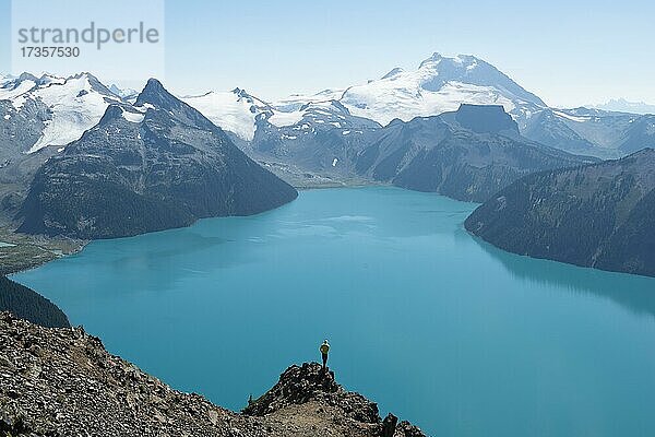 Junger Mann steht auf einem Felsen  blickt in die Ferne  Blick auf Berge und Gletscher mit türkisblauem See Garibaldi Lake  Gipfel Panorama Ridge  Guard Mountain und Deception Peak  Garibaldi Provincial Park  British Columbia  Kanada  Nordamerika