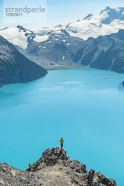 Junger Mann steht auf einem Felsen  blickt in die Ferne  Blick auf Berge und Gletscher mit türkisblauem See Garibaldi Lake  Gipfel Panorama Ridge  Guard Mountain und Deception Peak  Garibaldi Provincial Park  British Columbia  Kanada  Nordamerika