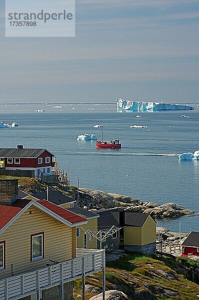 Wohnhäuser aus Holz vor einer Bucht mit Fischerboot und Eisbergen  Arktis  Diskobucht  Ilulissat  Grönland  Dänemark  Nordamerika