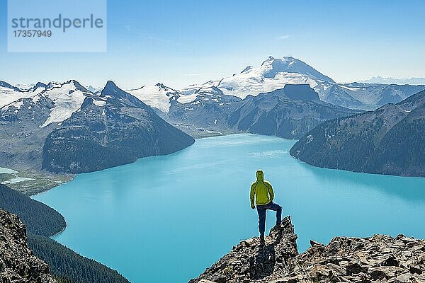 Junger Mann steht auf einem Felsen  blickt in die Ferne  Blick auf Berge und Gletscher mit türkisblauem See Garibaldi Lake  Gipfel Panorama Ridge  Guard Mountain und Deception Peak  Garibaldi Provincial Park  British Columbia  Kanada  Nordamerika