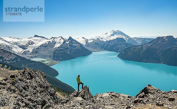 Junger Mann steht auf einem Felsen  blickt in die Ferne  Blick auf Berge und Gletscher mit türkisblauem See Garibaldi Lake  Gipfel Panorama Ridge  Guard Mountain und Deception Peak  Garibaldi Provincial Park  British Columbia  Kanada  Nordamerika