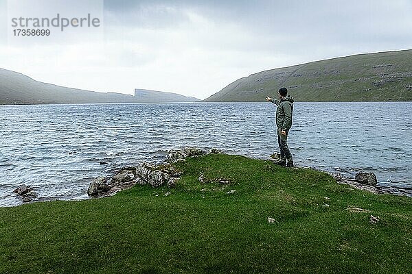 Wanderer steht am Ufer des Leitisvatn Sees und Zeigt in die Ferne  Vagar  Faroer Inseln