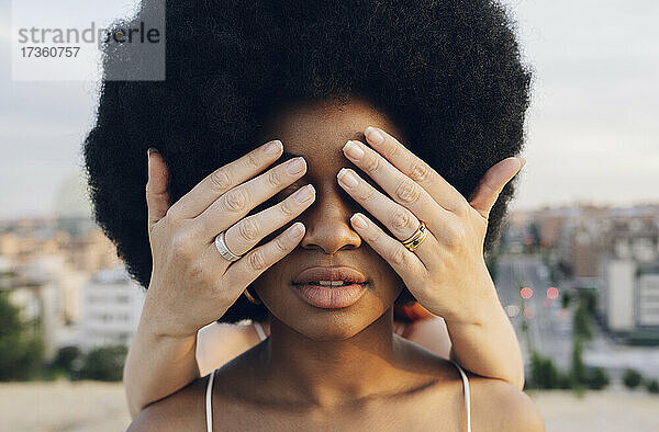 Frau bedeckt die Augen ihrer Afro-Freundin mit den Händen bei Sonnenuntergang