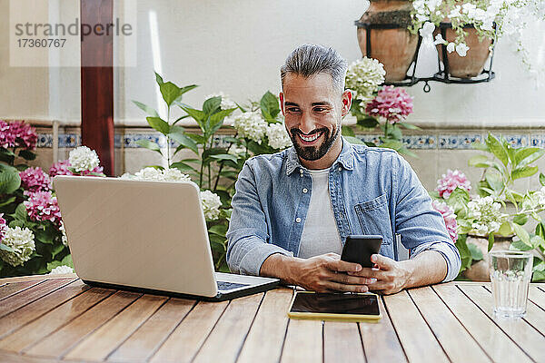 Lächelnde männliche Fachkraft  die während eines Videogesprächs über einen Laptop im Hinterhof spricht