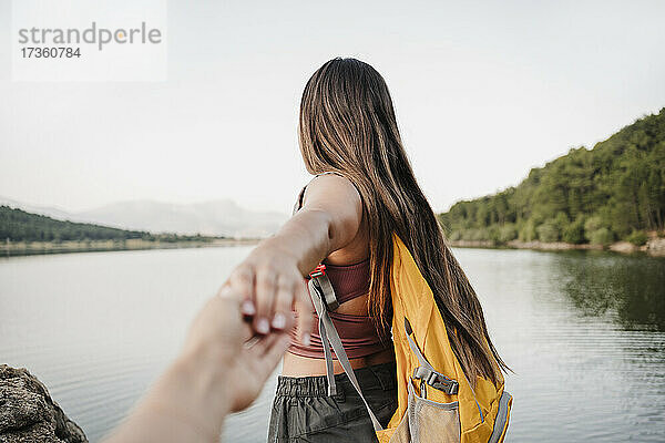 Weibliche Rucksacktouristin hält die Hand ihres Freundes am Seeufer
