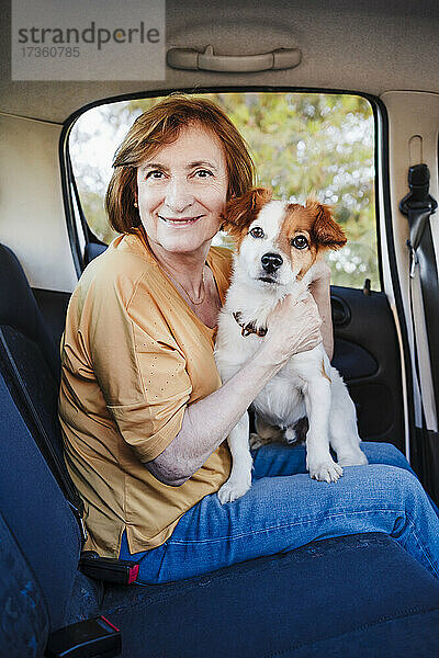 Frau sitzt mit Hund auf dem Rücksitz eines Autos