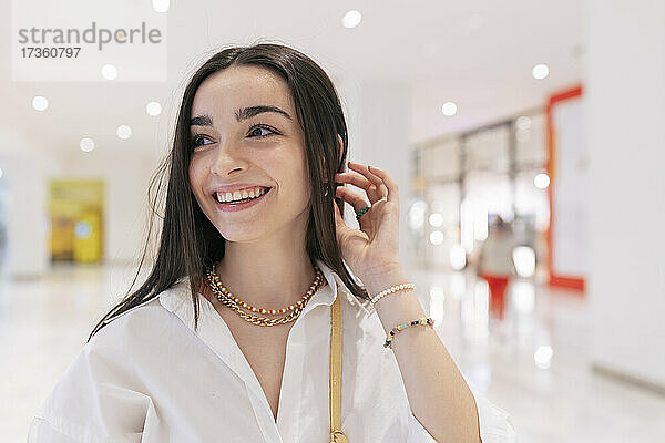 Lächelndes Teenager-Mädchen mit Hand im Haar  das im Einkaufszentrum wegschaut