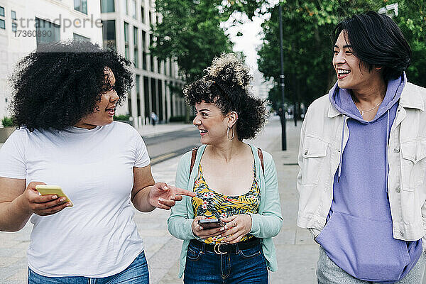 Multi-ethnische männliche und weibliche Freunde  die sich beim Gehen auf der Straße miteinander unterhalten