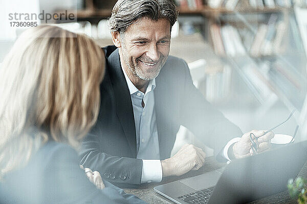 Lächelnder reifer Geschäftsmann  der mit einer Kollegin über einem Laptop in einem Café diskutiert