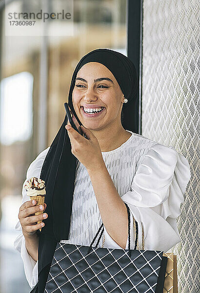Frau mit Eis lachend  während sie im Korridor mit ihrem Smartphone telefoniert
