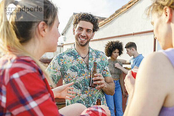 Junge männliche und weibliche Freunde  die während einer Party auf dem Dach etwas trinken