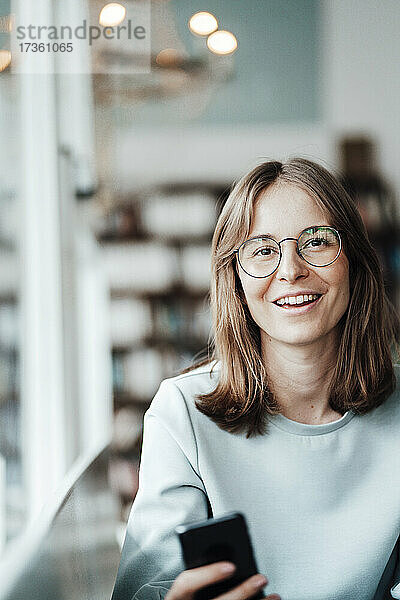 Glückliche junge Frau mit braunen Haaren und Brille in einem Café sitzend
