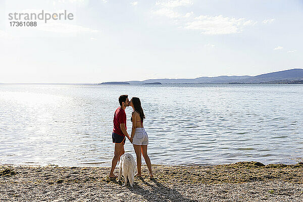 Paar  das sich küsst  während es bei einem Haustier am Seeufer steht