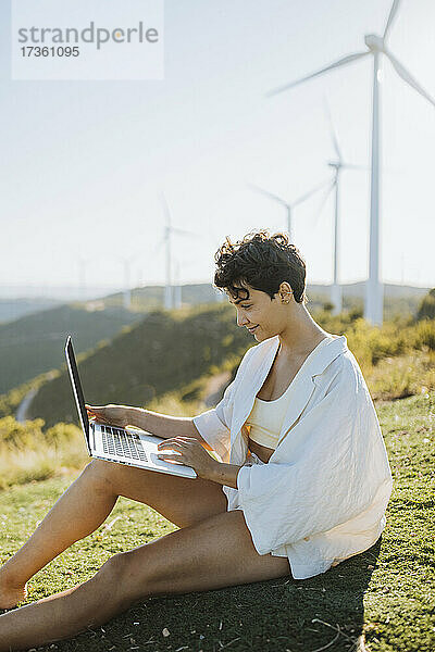 Lächelnde Frau  die einen Laptop benutzt  während sie auf einem Berg sitzt