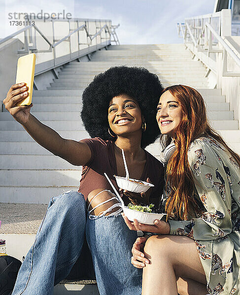 Lächelnde Afro-Frau macht Selfie mit Freundin auf Stufen