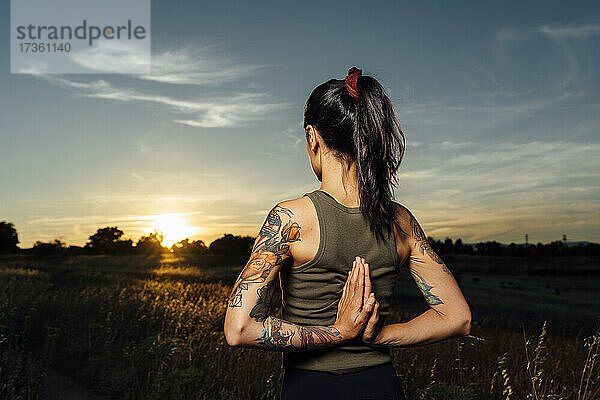 Frau mit hinter dem Rücken verschränkten Händen übt Yoga auf dem Lande