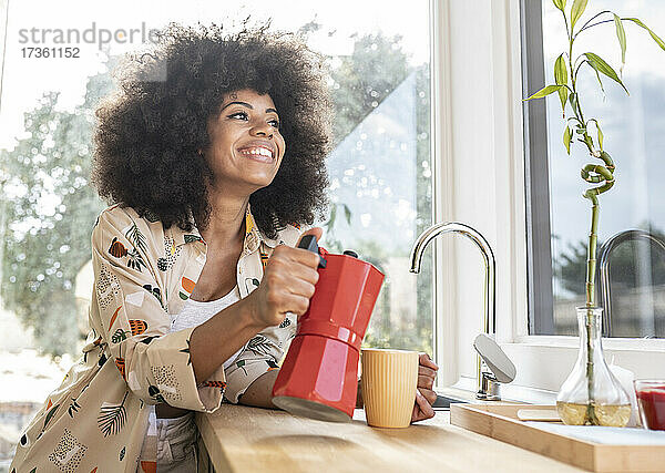 Afro-Frau gießt Kaffee aus dem Wasserkocher in einen Becher auf dem Küchentisch zu Hause