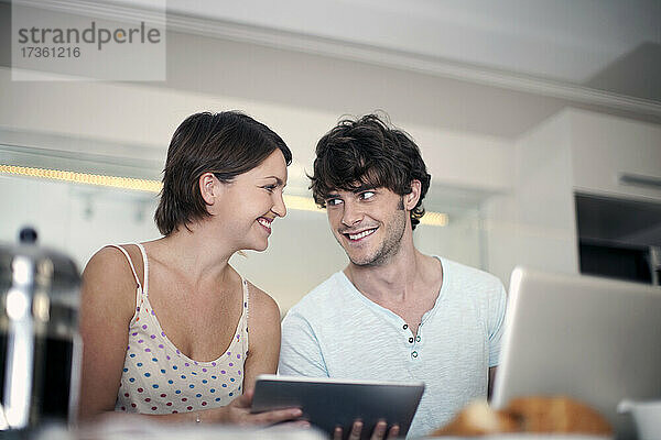 Lächelndes junges Paar sieht sich in der Küche sitzend an