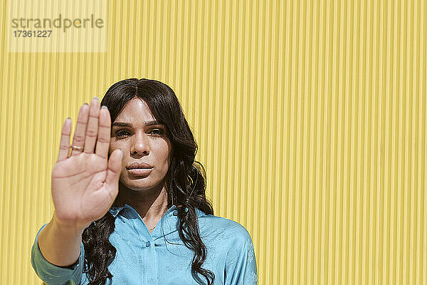 Nicht-binäre Frau zeigt Stopp-Geste vor gelber Wand