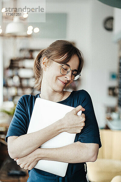 Lächelnde Freiberuflerin  die ihren Laptop umarmt  während sie in einem Cafe steht