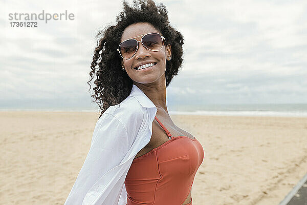 Lächelnde junge Frau  die wegschaut  während sie am Strand steht