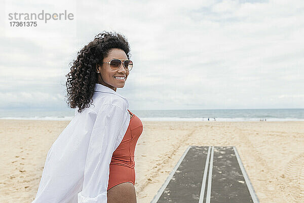 Lächelnde junge Frau mit Sonnenbrille am Strand
