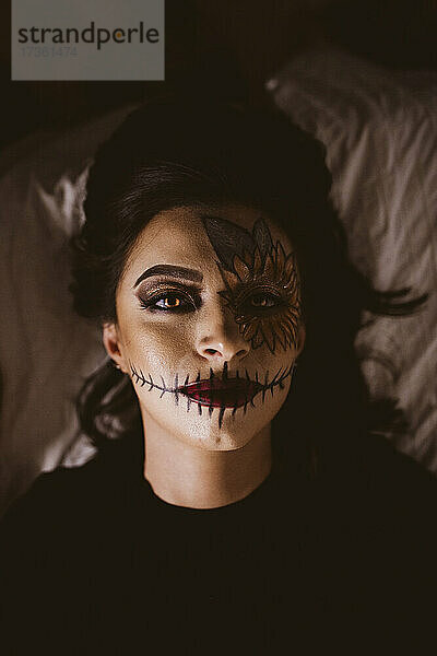 Frau mit zeremoniellem Make-up liegt zu Halloween auf dem Bett