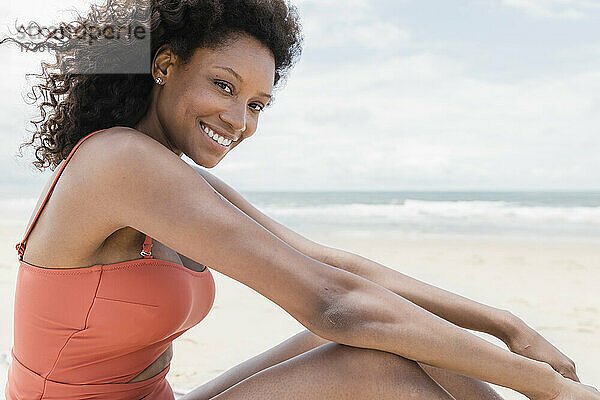 Glückliche junge Frau im Badeanzug am Strand sitzend