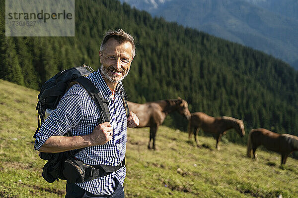 Lächelnder männlicher Wanderer mit Rucksack auf einem Berg stehend