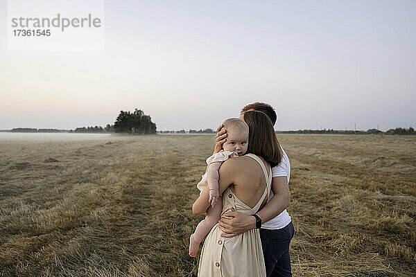 Mutter trägt süßes Mädchen  während sie neben einem Mann auf einem Feld steht