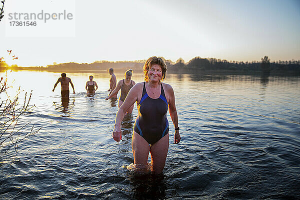Lächelnde reife Frau im Wasser stehend mit männlichen und weiblichen Freunden im Hintergrund