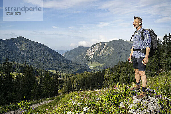Männlicher Wanderer mit Rucksack  der die malerische Landschaft vom Berg aus betrachtet