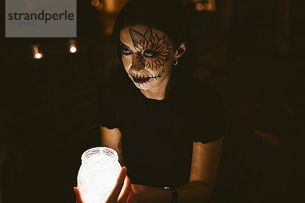 Frau hält beleuchtetes Glas mit Freund bei Nacht während Halloween