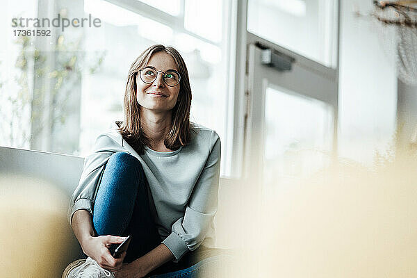Lächelnde Frau mit Brille  die wegschaut  während sie in einem Cafe sitzt