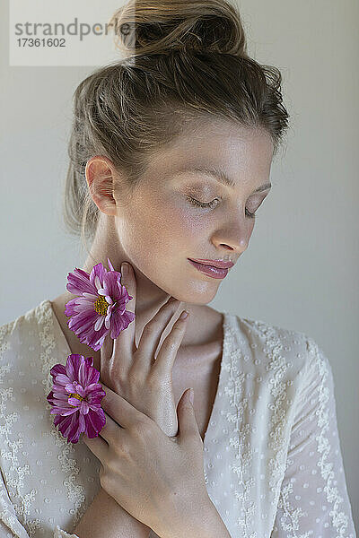 Junge schöne Frau mit geschlossenen Augen hält lila Gänseblümchen vor weißem Hintergrund