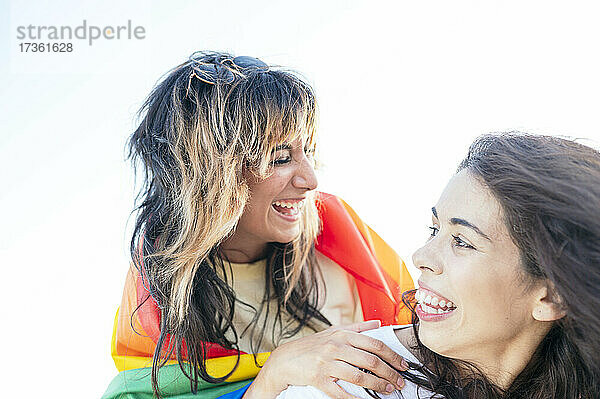 Frau mit Regenbogenflagge lacht  während sie ihre Freundin anschaut